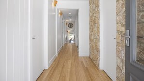 A hallway with wooden flooring, white walls, and a stone accent wall. - Saltwood Coastal Hamptons Luxe With Pool (Melbourne)