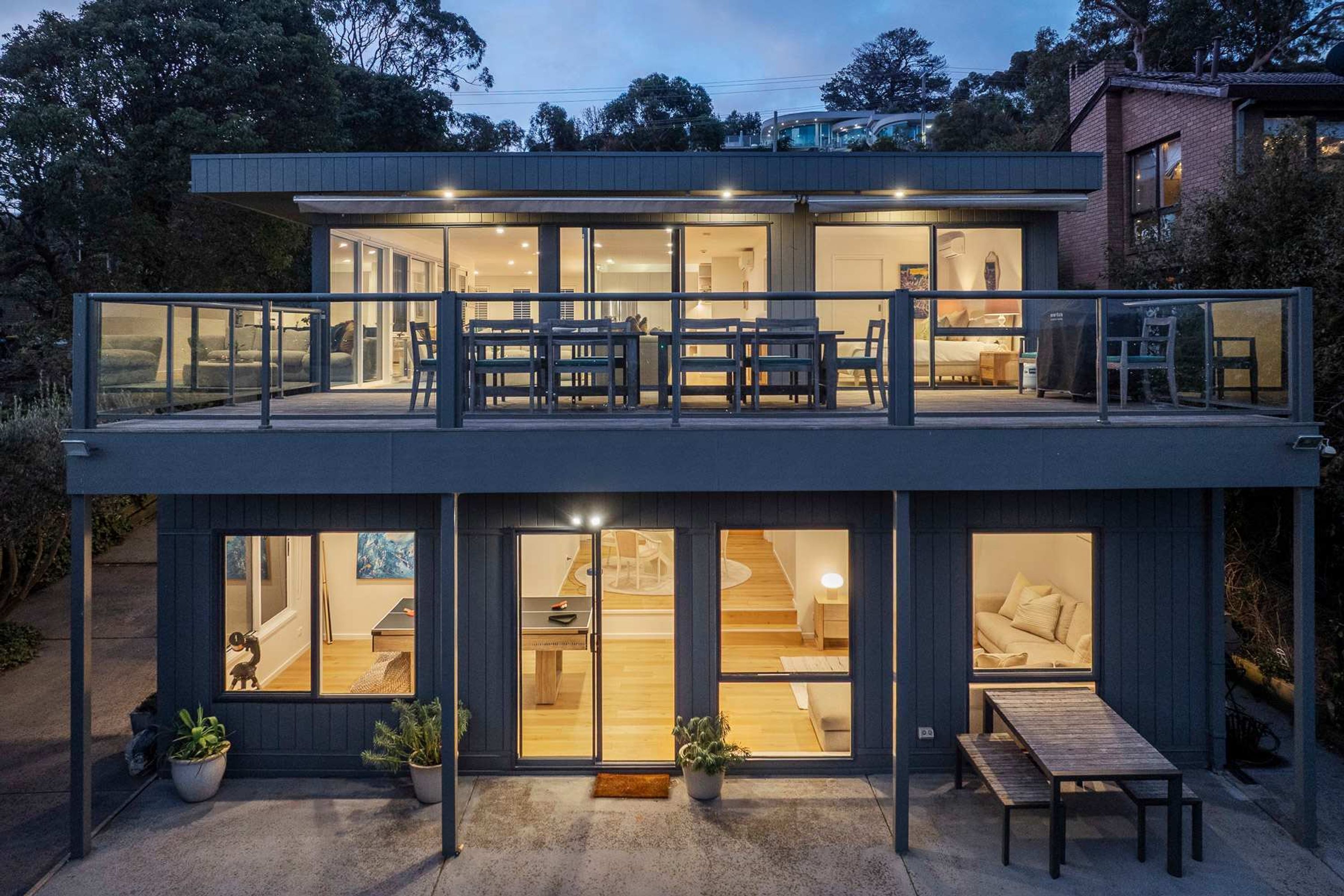 Une maison moderne à deux étages, dotée d’un balcon, de grandes fenêtres et d’un intérieur bien éclairé.