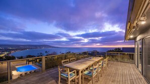 A wooden deck with a pool and dining area overlooking a body of water at dusk. - Martha s Peak Heated Pool Views (Melbourne)