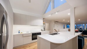A modern kitchen with white cabinetry, a central island, and a view of the city through large windows. - Martha s Peak Heated Pool Views (Melbourne)