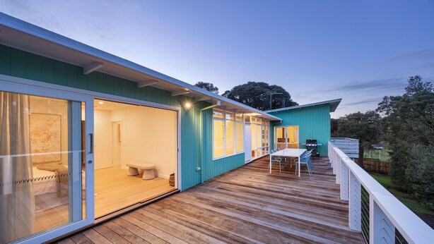 Una casa moderna con terraza de madera, amplios ventanales y zona de comedor.