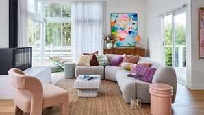 Una sala de estar moderna con un sofá grande, un sillón rosa, una mesa de centro y una televisión.