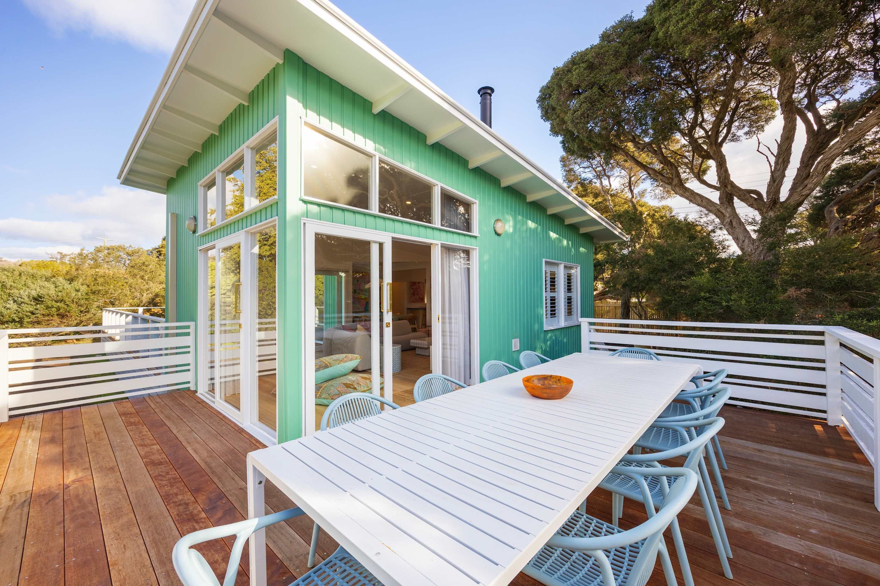 A turquoise house with a deck, white exterior, and a large table with chairs.