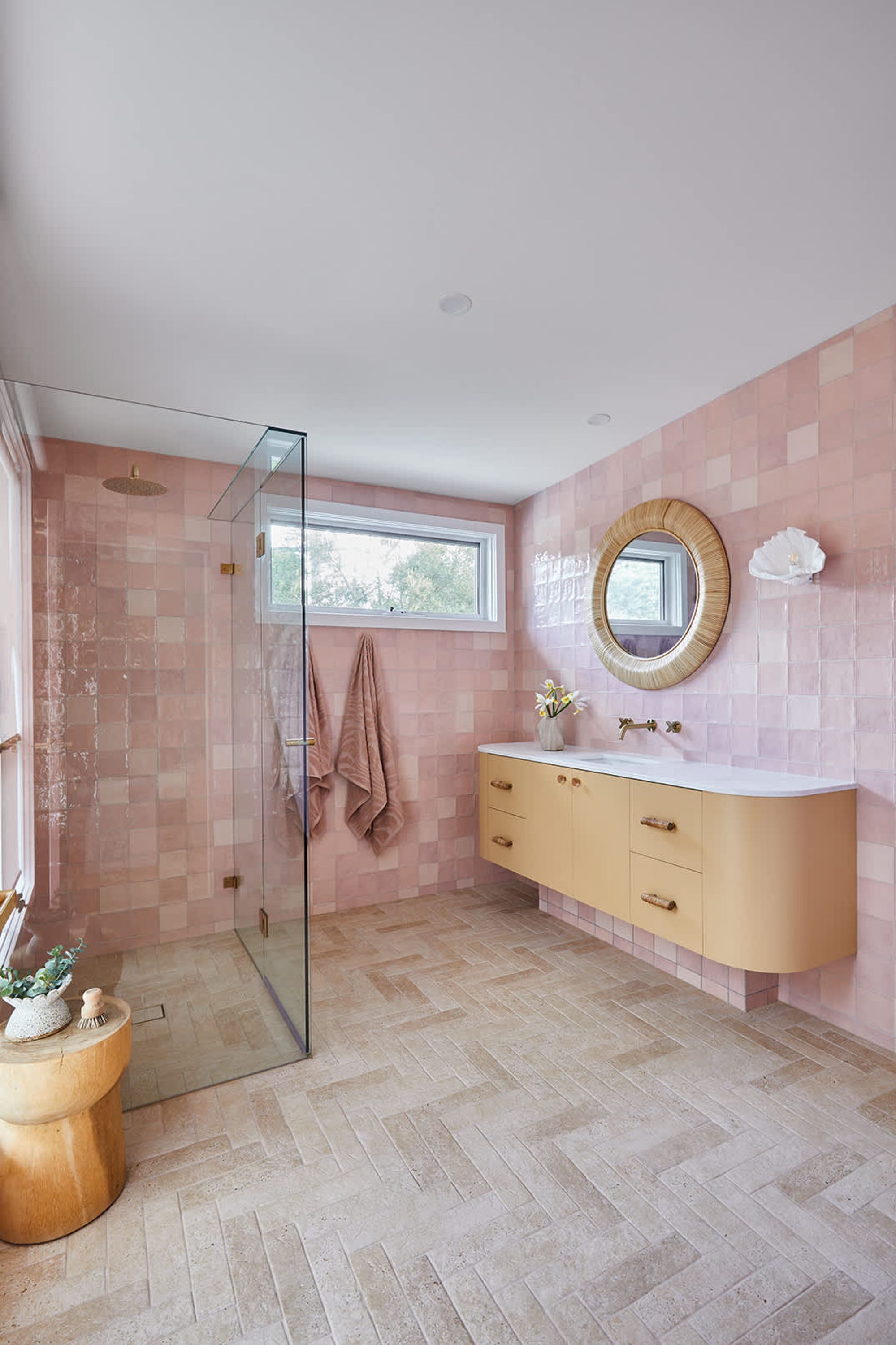 A bathroom with a glass shower enclosure, a vanity with a round mirror, and a window above the sink.