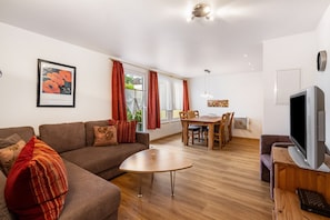 Un salon moderne comprenant un canapé, une table basse, un coin repas avec une table et des chaises, et un téléviseur posé sur un meuble en bois.