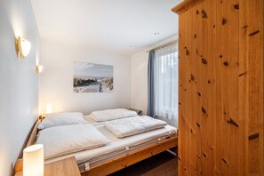 Une chambre à coucher avec un lit en bois, deux oreillers blancs, une table de chevet avec une lampe, un tableau au mur et une armoire en bois.