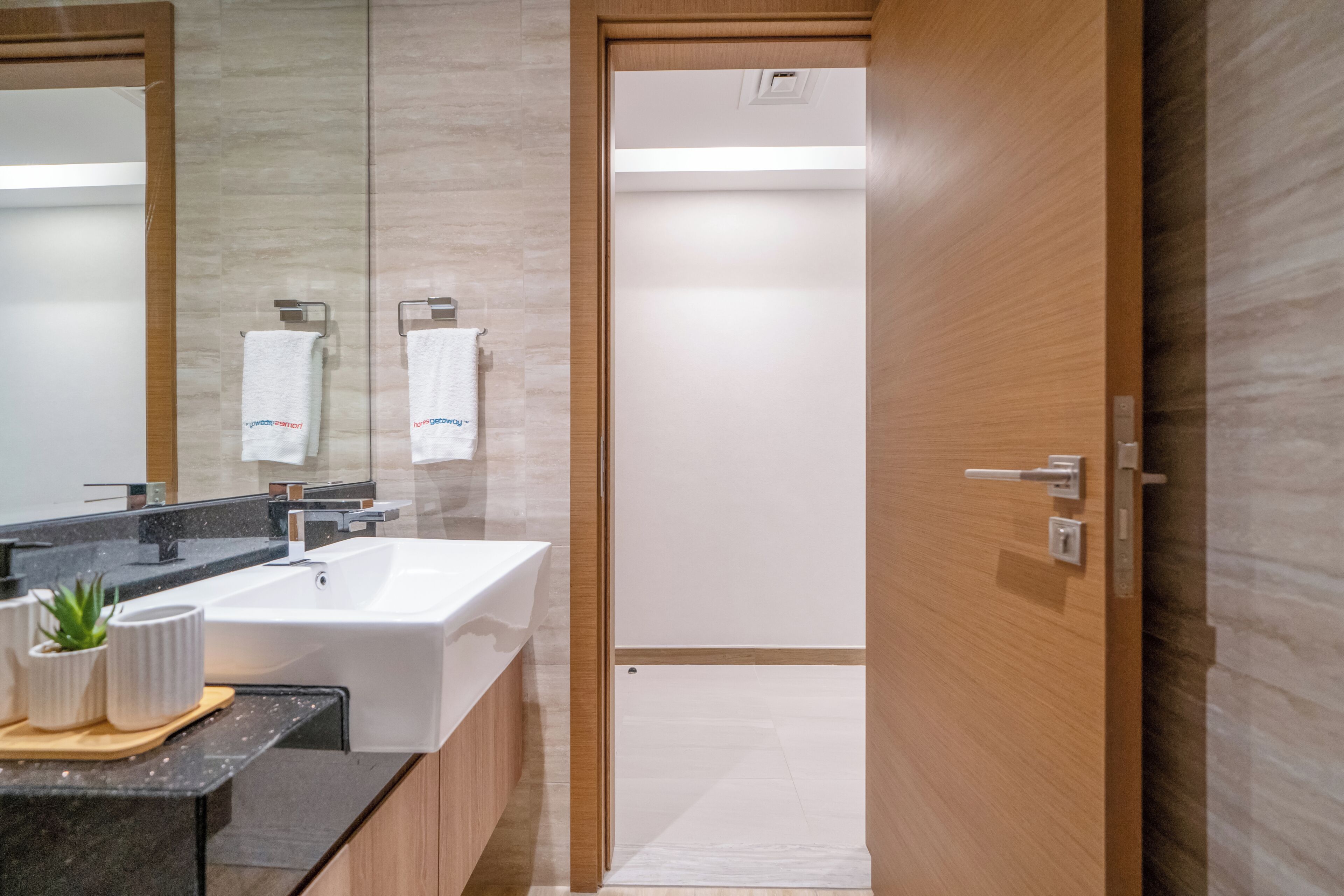A modern bathroom with a large mirror, white sink, and wooden door.