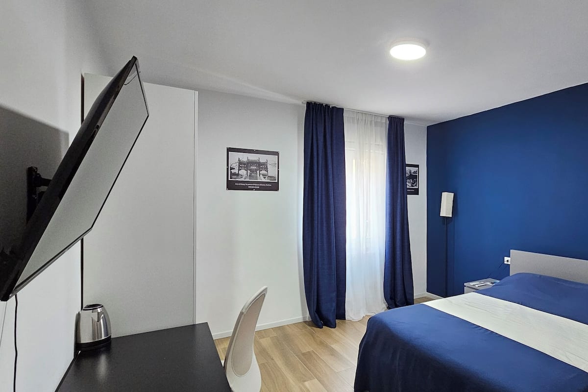 A hotel room with a bed, a desk, a chair, a TV, and a nightstand.