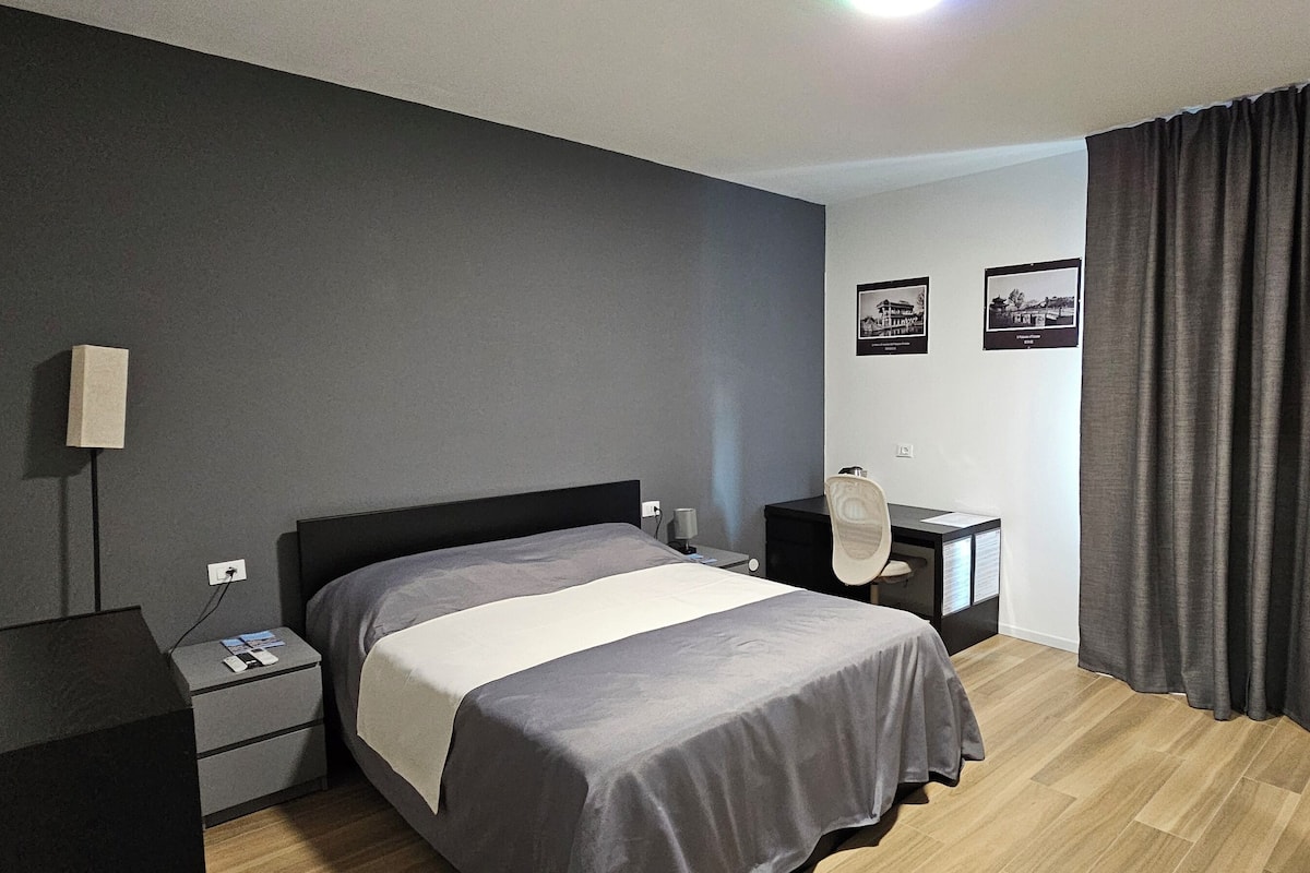 A modern bedroom with a bed, bedside tables, a desk, and a chair.