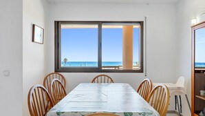Un coin repas avec une table et des chaises, une fenêtre donnant sur la plage et un buffet contenant de la vaisselle.