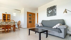 Un salon comprenant un canapé, une table basse, une table à manger avec des chaises, un meuble et une horloge murale.