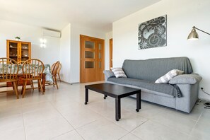 Una sala de estar con un sofá, una mesa de centro, una mesa de comedor con sillas, un mueble aparador y un reloj de pared.