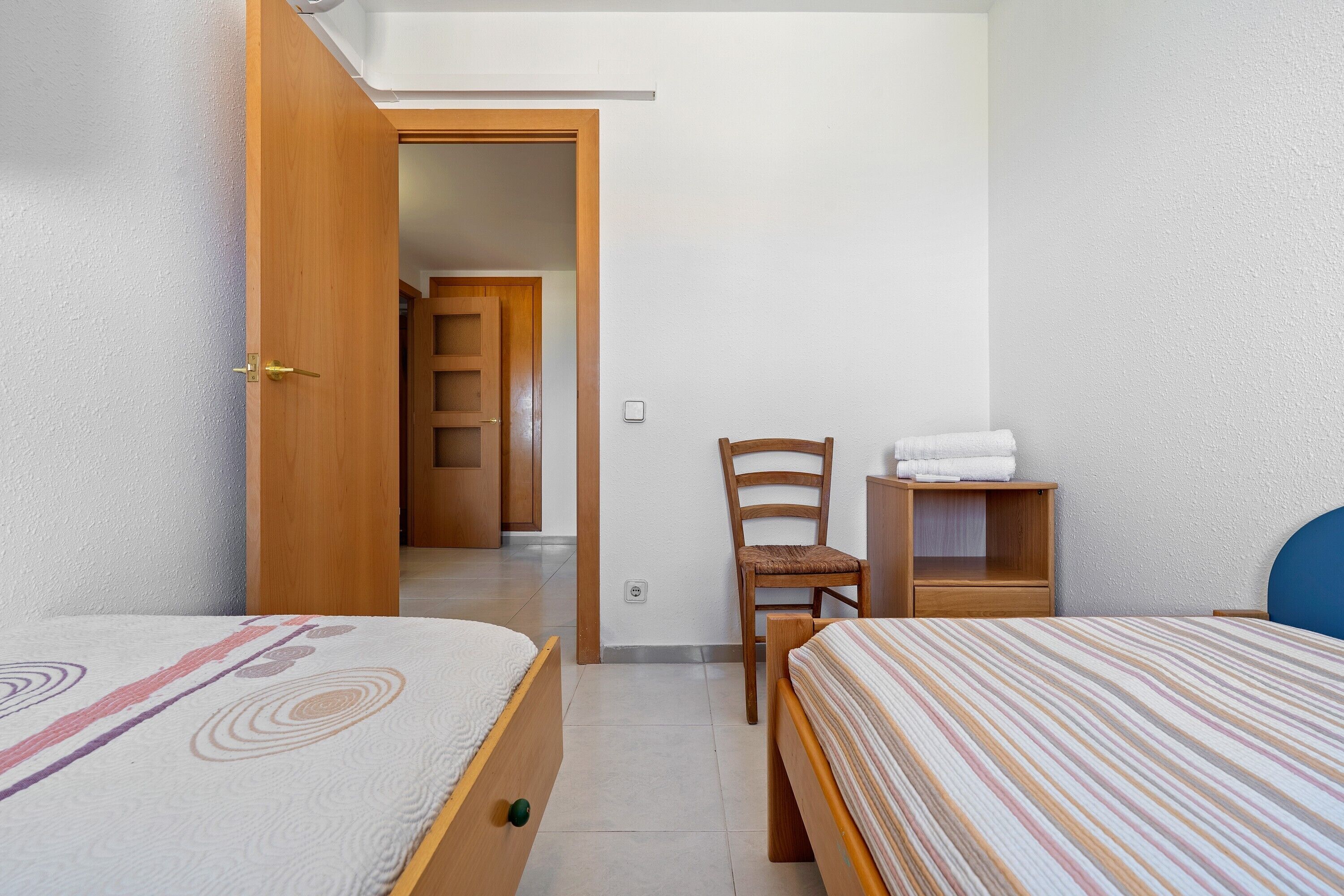 A bedroom with two beds, a wooden chair, a nightstand, and a door leading to another room.