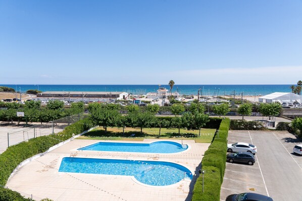 A swimming pool with a view of the sea, a parking lot, and a building in the background.