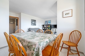 Un comedor con una mesa cubierta por un mantel estampado con motivos de hojas, rodeado de sillas de madera.