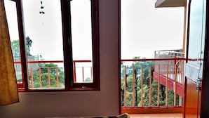 A room with a bed, a window with a view of a balcony, and a hanging ornament.