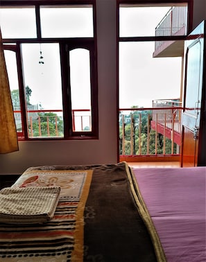 Ein Zimmer mit einem Bett, einem Fenster mit Blick auf einen Balkon und einem hängenden Ornament.