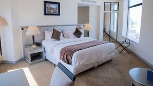 A hotel room with a large bed, bedside lamps, a small table, a chair, and a window with a view.
