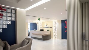 A hotel reception area with a reception desk, a blue wall with decorative glass panels, and a seating area with a chair.