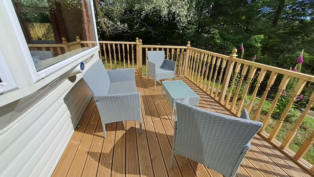 A wooden deck with wicker chairs and a table, surrounded by a wooden railing. - The Lookout - Park Home, Farm Park Stay (Swansea)