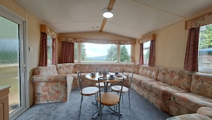 A caravan interior with a sofa set, a dining table, and chairs. - The Lookout - Park Home, Farm Park Stay (Swansea)