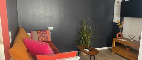 A modern living room with a grey accent wall, a white sofa with colorful cushions, a small wooden side table, and a potted plant.