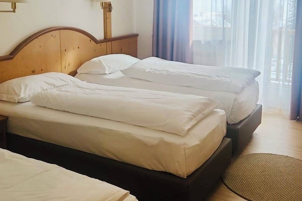 A hotel room with two beds, wooden headboards, a large window with curtains, and a wooden floor.