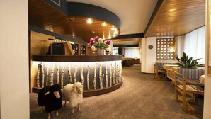 A hotel lobby with a curved reception desk, seating area, and a decorative wall with wooden branches. - HOTEL VILLA ROSA (Campitello di Fassa)