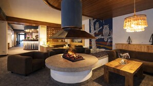 A modern interior with a central stone fire feature, a wooden ceiling, and a seating area with sofas and a table. - HOTEL VILLA ROSA (Campitello di Fassa)