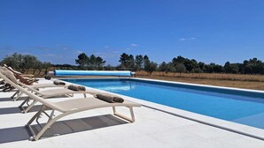 Ein Poolbereich mit Liegestühlen und wolkenlosem, blauem Himmel.