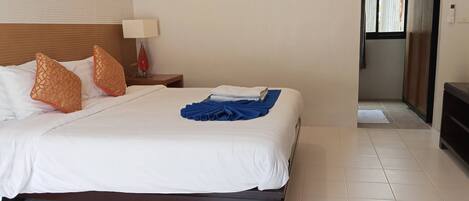 A hotel room with a neatly made bed, a bedside lamp, and a view of the hallway.