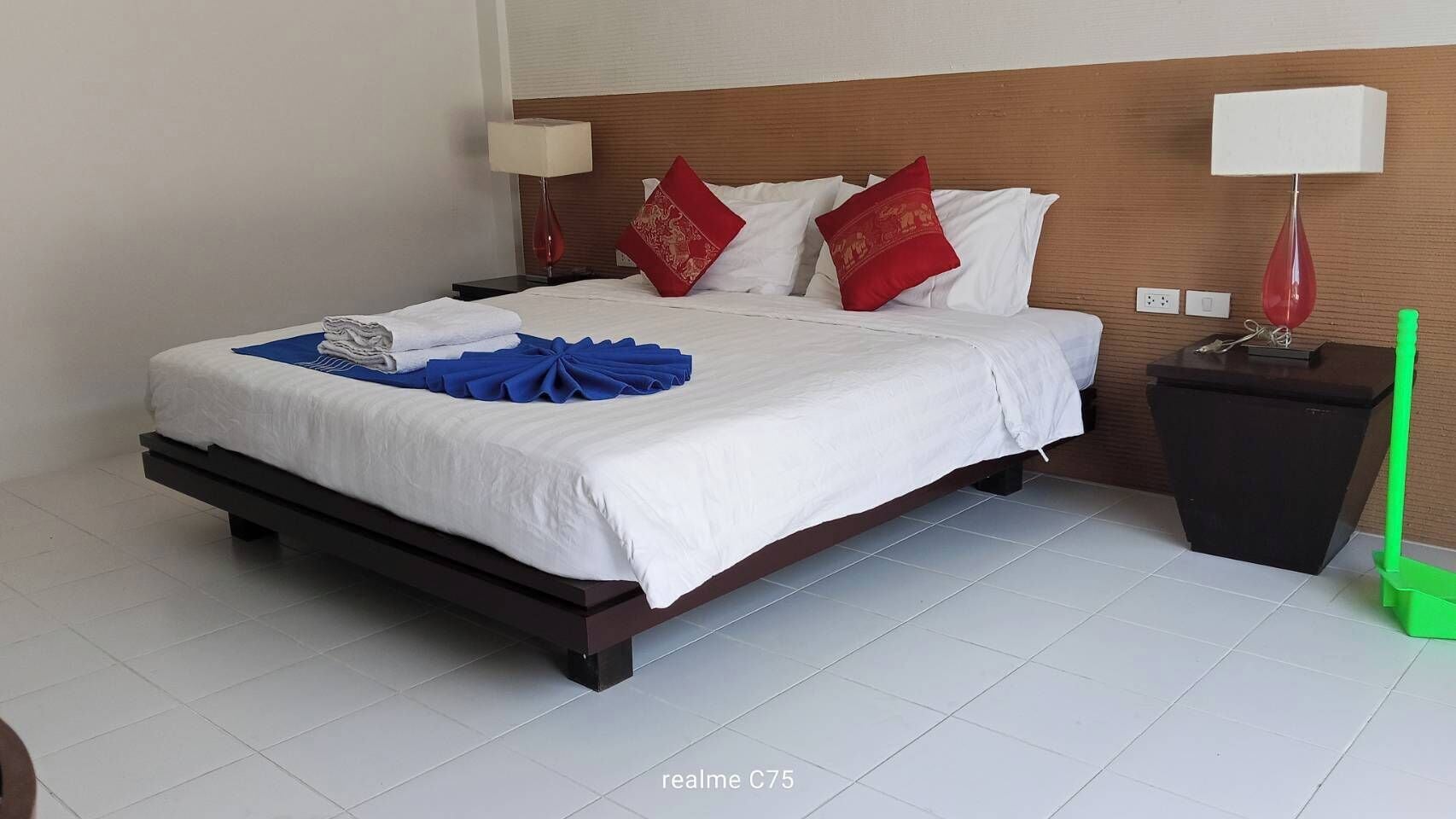 Habitació d'hotel amb un llit, dues taules de nit, una petita taula auxiliar, una eina de neteja verda i un paviment de rajoles blanques.
