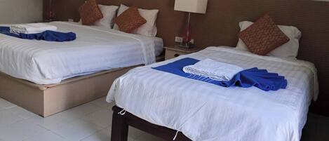 A hotel room with two beds, each with white linens and brown patterned pillows. There are folded towels and a blue blanket on one bed.