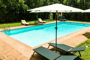 A rectangular swimming pool with a tiled deck, surrounded by lounge chairs and umbrellas.