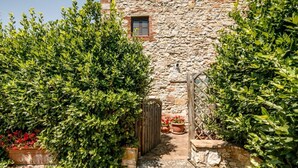 Ein Steinhaus mit einem hölzernen Tor, umgeben von üppigem Grün und Kübelpflanzen.