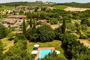 Una villa con piscina rodeada de árboles y un viñedo al fondo.