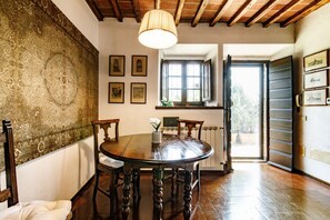 Un comedor con una mesa redonda de madera, sillas, una lámpara colgante y una ventana con contraventanas abiertas.