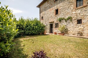 Un bâtiment en pierre doté d’un jardin, d’une porte et de fenêtres.