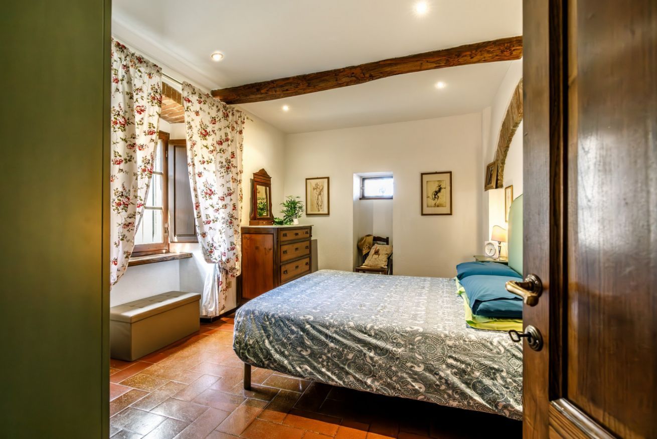 Een slaapkamer met een bed, een kaptafel, een raam met gordijnen, een nachtkastje en een deur.