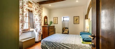 A bedroom with a bed, a dresser, a window with curtains, a bedside table, and a door.