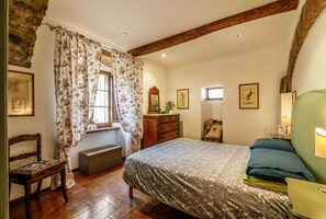 A bedroom with a bed, a chair, a window with curtains, a dresser, and wall art.