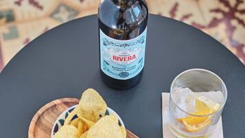 A bottle of Rivera wine, a bowl of chips, a glass with an orange slice, and a bowl of olives on a round table.