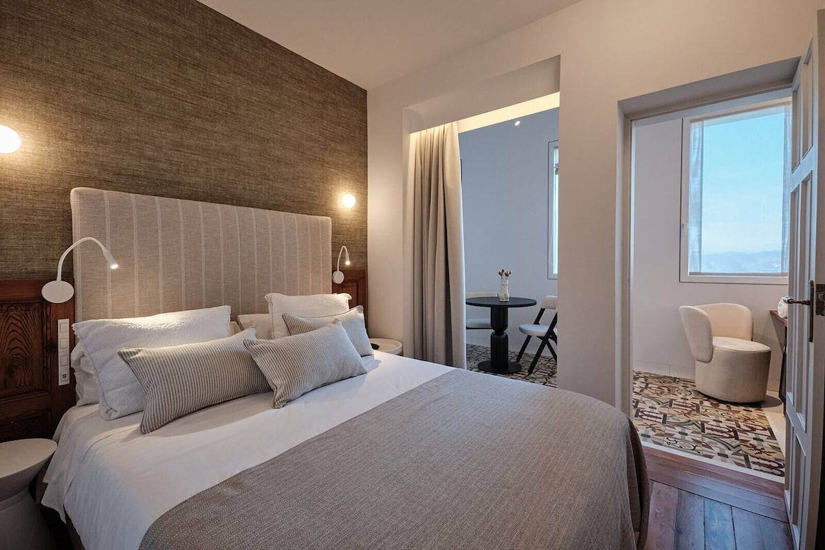 Une chambre d’hôtel avec un grand lit, des lampes de chevet, une vue sur le balcon et un fauteuil près de la fenêtre.
