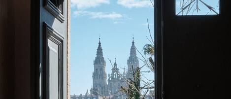 A view through a window of a building with two prominent spires, likely a cathedral or church, with a clear sky and some foliage in the foreground.