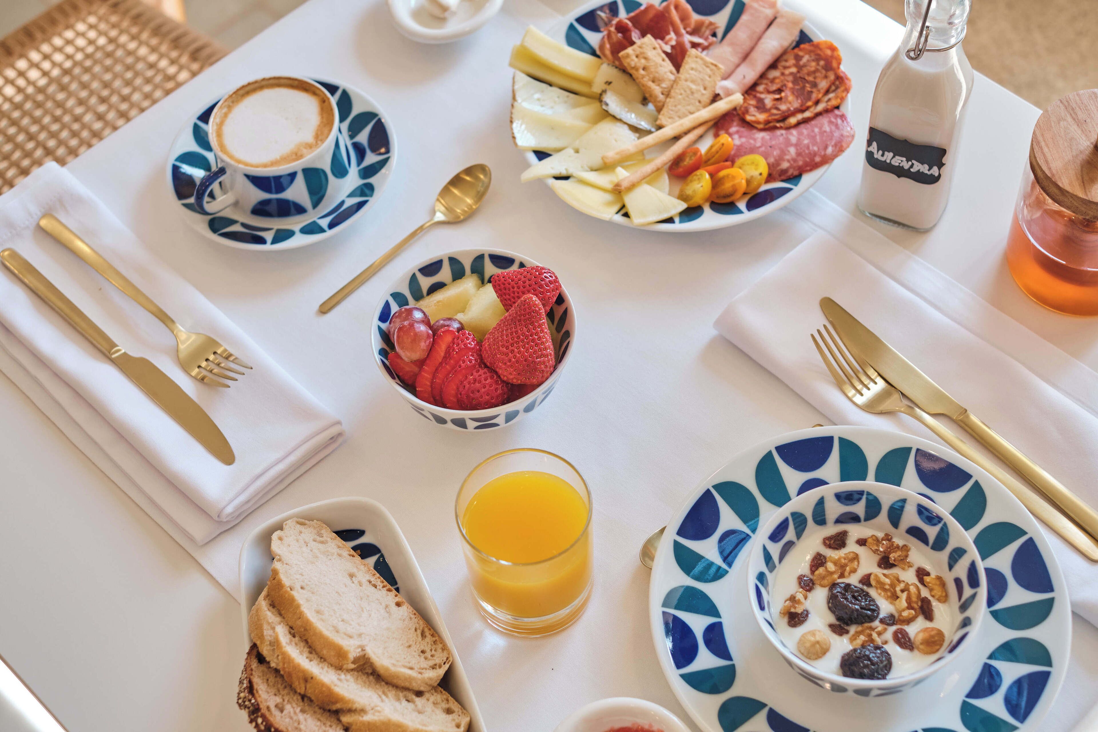 Una mesa de desayuno con platos de comida, un vaso de jugo de naranja y una botella de leche.