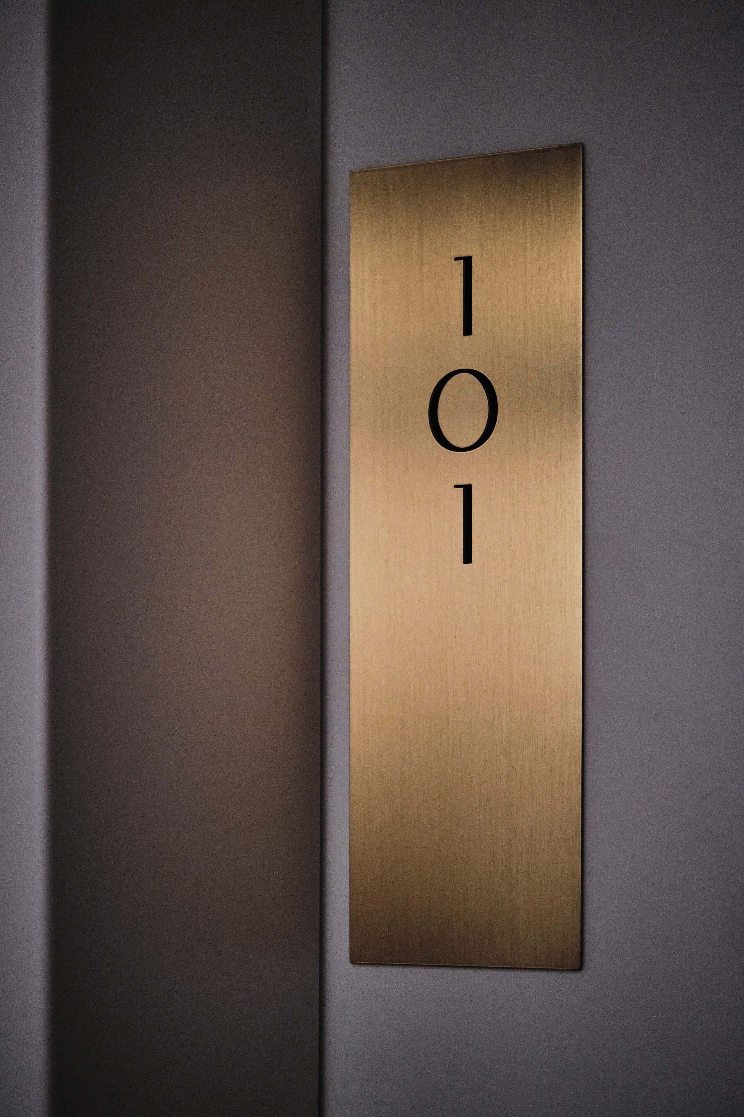 A metallic room number plaque with the numbers "101" mounted on a wall.
