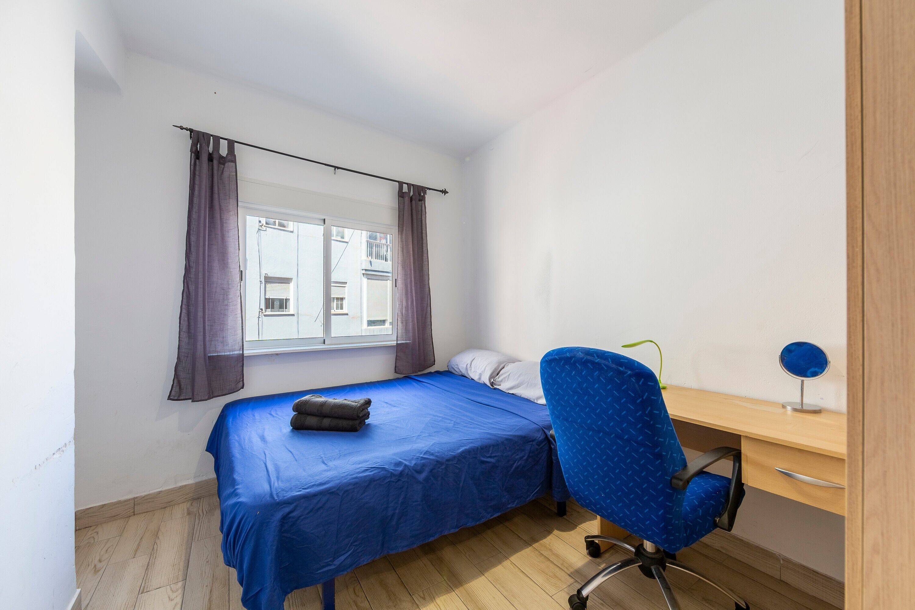 A bedroom with a single bed, a desk, a chair, and a window with curtains.