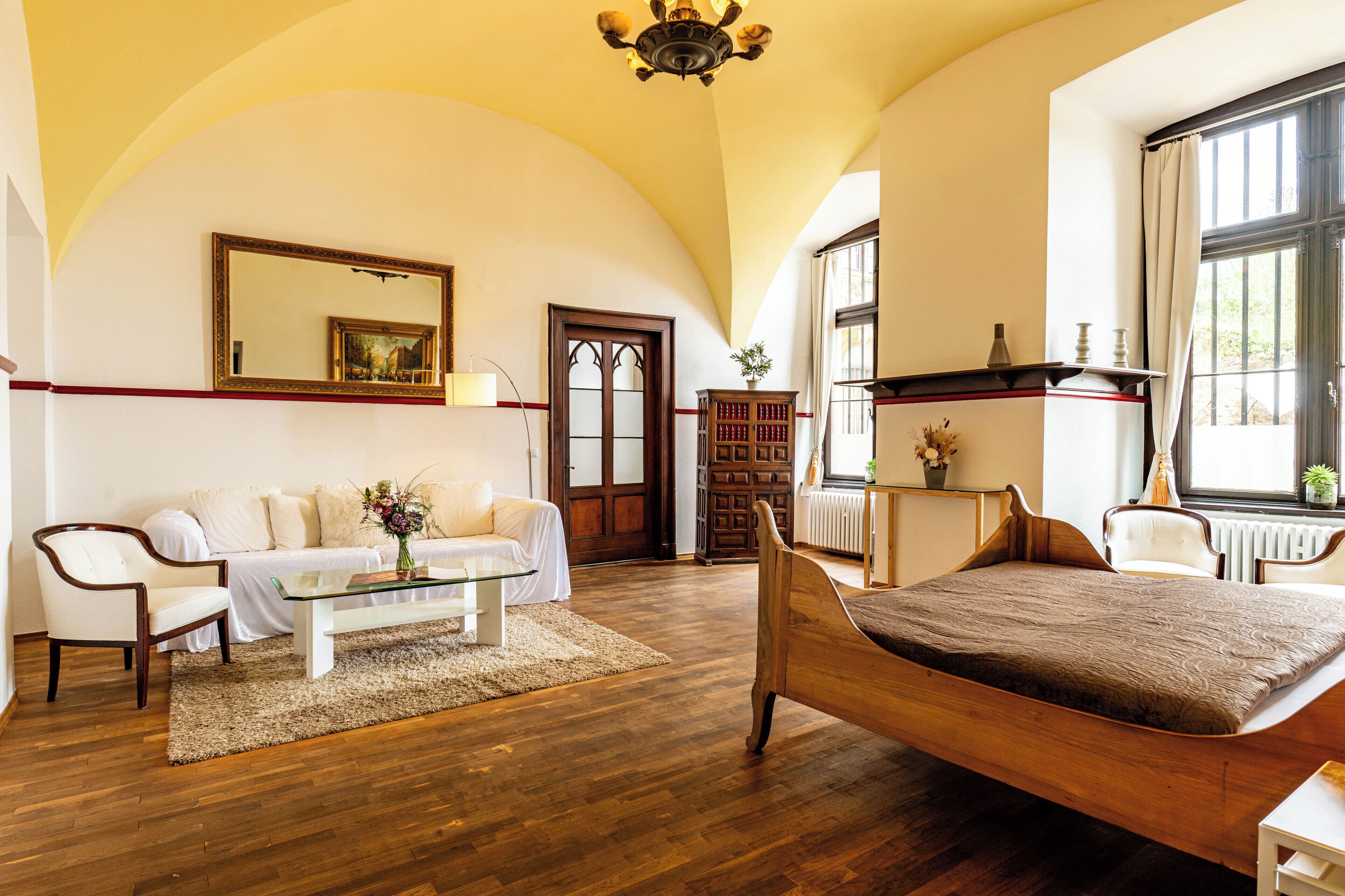 A spacious room with a wooden bed, a white sofa, a glass coffee table, and a large mirror.