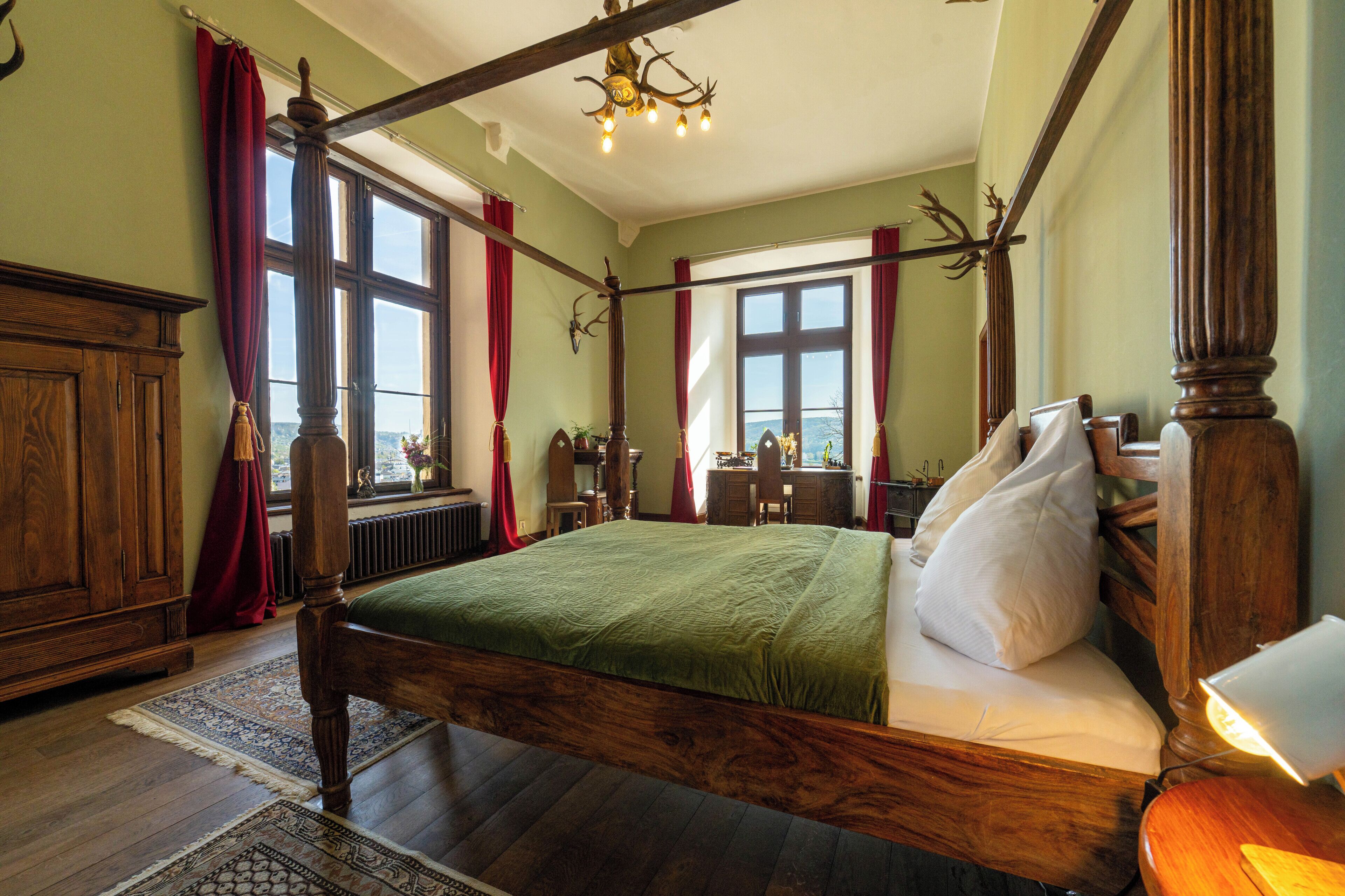 A traditional bedroom with a large bed, wooden furniture, and a view through the window.