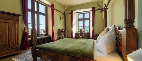 A traditional bedroom with a large bed, wooden furniture, and a view through the window.